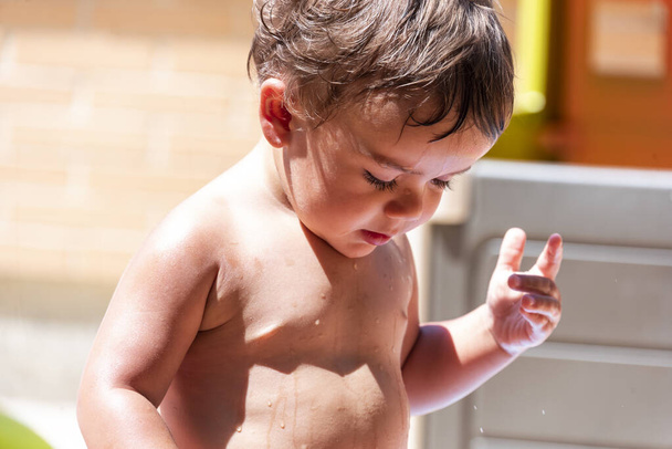 Happy little boy playing with water hose in the backyard - Photo, Image