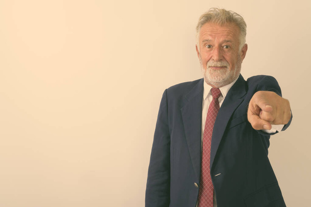 Studio shot of handsome senior bearded businessman pointing at camera against white background - Фото, изображение