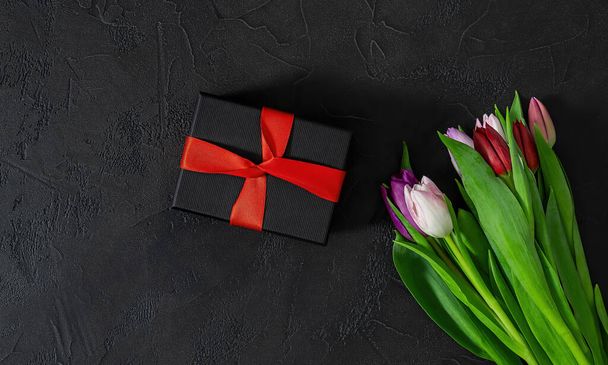 Gelukkige Valentijnsdag, Vrouwendag, Moederdag concept. Cadeaudoosje en tulpenbloemen op zwarte achtergrond, kopieer ruimte voor je tekst. - Foto, afbeelding