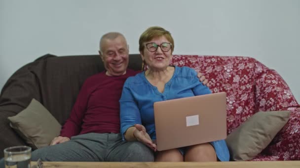 Vanhempi nainen käyttää läppäriä ja hymyilee iloisesti. Mies istuu hänen vieressään ja jatkaa keskustelua.. - Materiaali, video