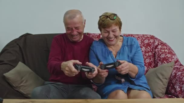 Oudere stel spelen thuis, zitten op de bank een videospel. Conceptietijd tijdens quarantaine. - Video