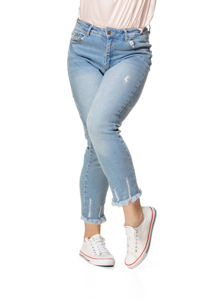 青いジーンズと白い背景に隔離されたスポーツシューズでスリム女性の足 - 写真・画像