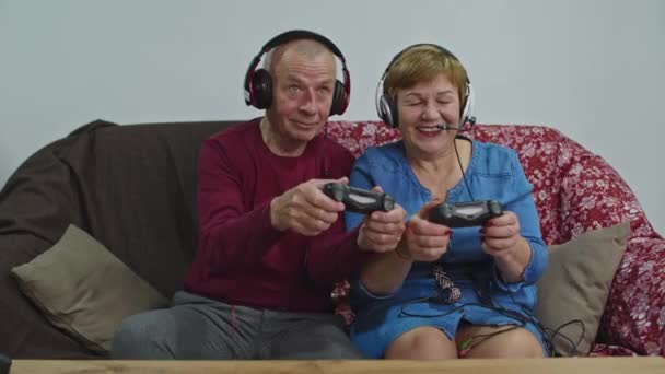 Senior koppel speelt videospel thuis met grote koptelefoon. Technologieconcept. - Video