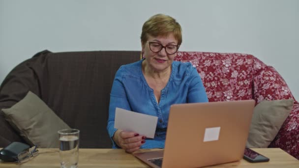 A woman pays for services while sitting at home on the couch at the computer. - Záběry, video