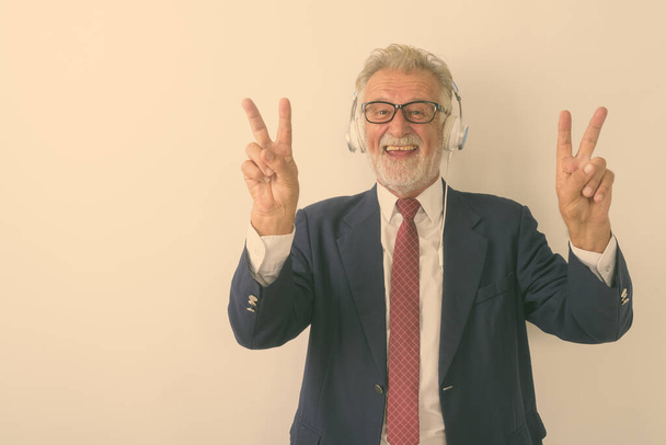Studio colpo di felice anziano barbuto uomo d'affari sorridente e dando segno di pace con entrambe le mani mentre si ascolta la musica su sfondo bianco - Foto, immagini