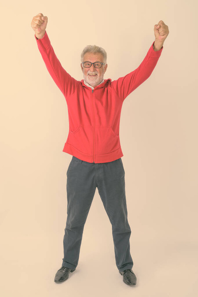 Ganzkörperaufnahme eines glücklichen älteren bärtigen Mannes, der im Stehen lächelt und vor weißem Hintergrund aufgeregt wirkt - Foto, Bild