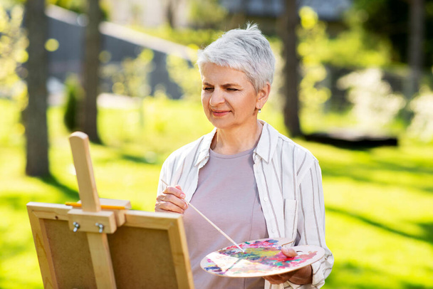senior woman with easel painting outdoors - Zdjęcie, obraz