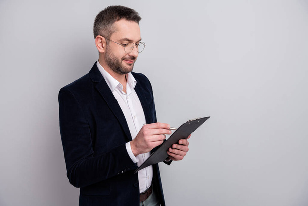 Close-up profile side view portrait of his he nice attractive focused mature man holding in hands clipboard writing recommending memo review isolated over light gray pastel color background - Φωτογραφία, εικόνα