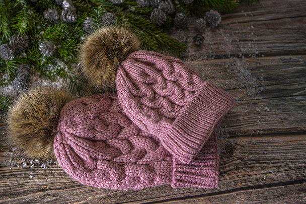 Warm knitted pink hats with pompom for mother and daughter. Christmas decoration on wooden background, flat lay.  - Photo, Image