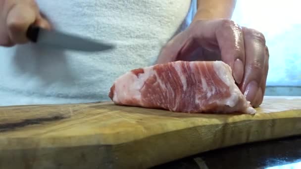 Жінка вирізає великий шматочок свинячого м'яса ножем. М'ясо з жирними шарами, свиняча шия
. - Кадри, відео