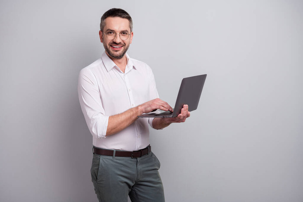 Portrait of his he nice attractive cheerful cheery successful mature man holding in hands laptop creating web design presentation isolated over light gray pastel color background - 写真・画像