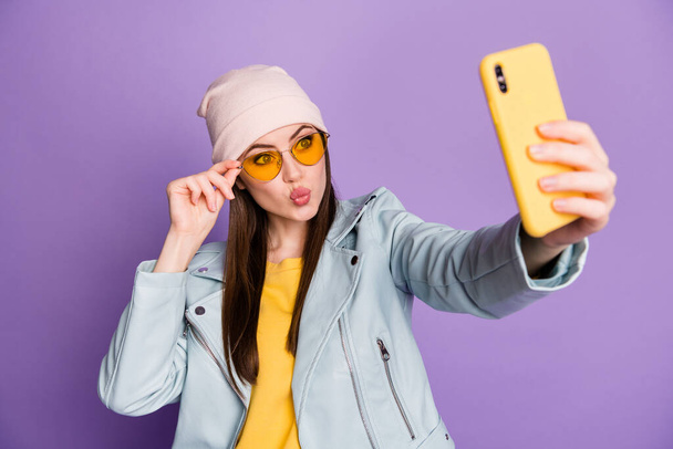 Photo of funny pretty youngster lady hold telephone make selfies popular blogger sending air kisses wear sun specs casual hat jacket yellow pullover isolated purple color background - Foto, imagen