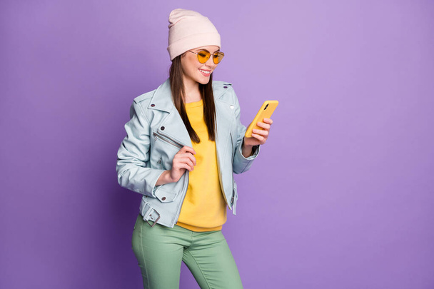 Profile photo of stylish pretty lady street look clothes hold telephone toothy smiling read news wear sun specs casual hat blue jacket pullover green pants isolated purple color background - Фото, изображение