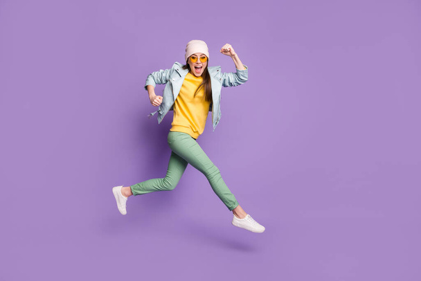 Full size profile side photo of amazed excited girl enjoy lottery discount win jump run fast speed wear green pants headwear sunglass isolated over violet color background - Photo, image