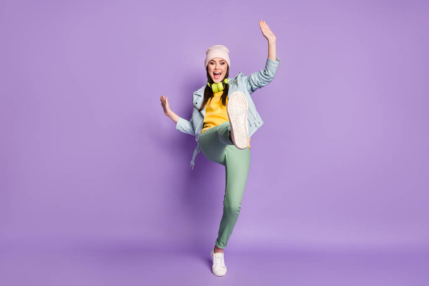 フルサイズの写真のクールなファンキーな女性の通りの服良い気分ダンス奇妙な若い動きを上げる足高着用カジュアル帽子ジャケットパンツシューズ隔離された紫の色の背景 - 写真・画像