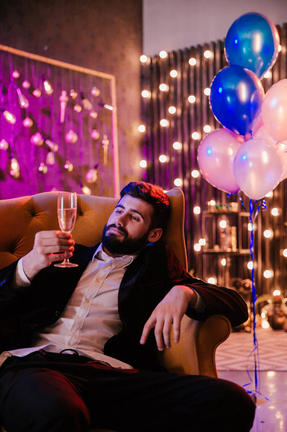 Przystojny młody facet w luźnym garniturze, cieszący się wieczorem na imprezie, pijący musujące wino tło, duża imprezowa atmosfera. - Zdjęcie, obraz
