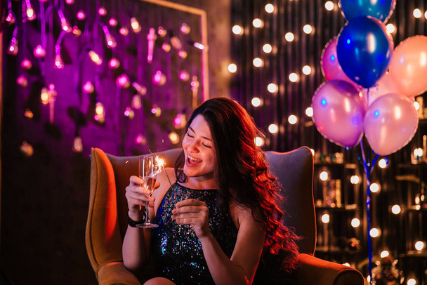 Jolie jeune femme devant la caméra sur le canapé elle profite de la fête d'anniversaire elle tient une coupe de champagne et scintille - Photo, image