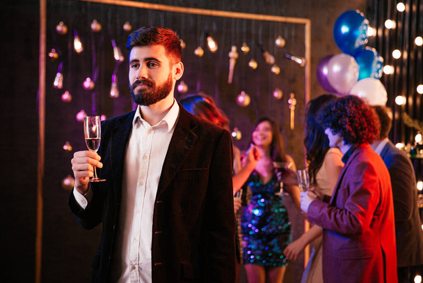Привабливий і смішний хлопець з кучерявим волоссям тримає келих шампанського перед камерою на великій вечірці він насолоджується моментом
 - Фото, зображення