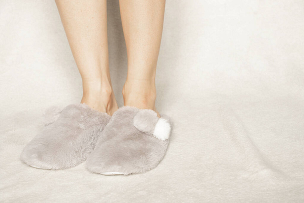 pies femeninos en pantuflas interiores grises en el suelo en casa en invierno - Foto, Imagen