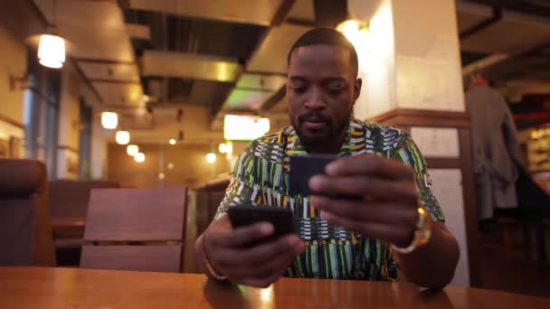 Afroamerican homme écrit nombre de carte de crédit dans le smartphone, services bancaires en ligne - Séquence, vidéo