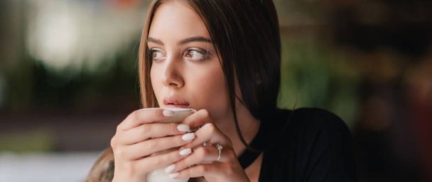 pretty young woman sitting in a cafe with a cup of coffee latte. Brunette girl in cafe with latte. - Foto, Bild