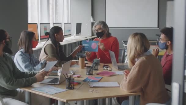 コロナウイルスのパンデミック時にオフィスミーティングを開催しながら、ビジネスプロジェクトを議論保護面マスクの多民族の同僚のチーム - 映像、動画