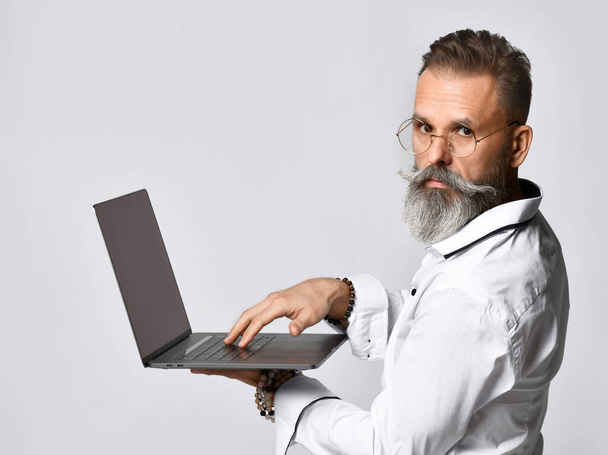 Studio πορτρέτο ενός μεσήλικα hipster άνθρωπος κρατώντας ένα φορητό υπολογιστή και κοιτάζοντας την κάμερα. - Φωτογραφία, εικόνα