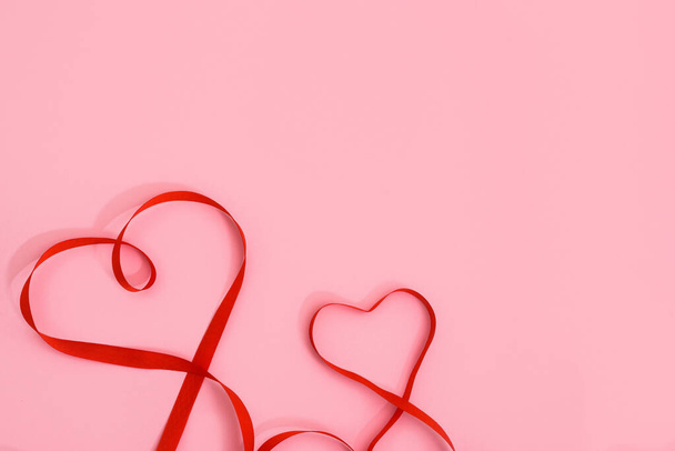 valentine's day red ribbon curves in the shape of a heart on a pink background. festive background for wedding and greeting cards, mockup, copy space. - Zdjęcie, obraz