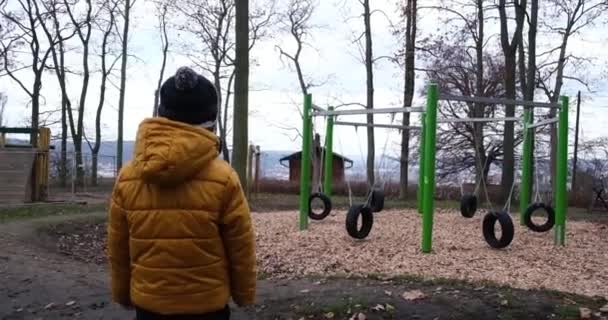 Swing σε άδειο παιδική χαρά καλύπτονται. Ένα μικρό αγόρι κοιτάζει μια άδεια παιδική χαρά - Πλάνα, βίντεο
