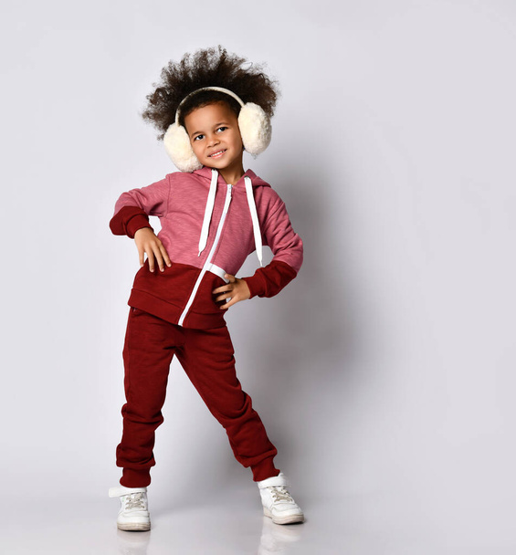 Happy smiling African American girl posing in warm headphones and sportswear. - Photo, Image