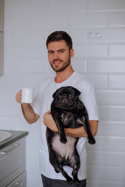 A man holds a pug dog in his arms, and drinks coffee - Fotó, kép