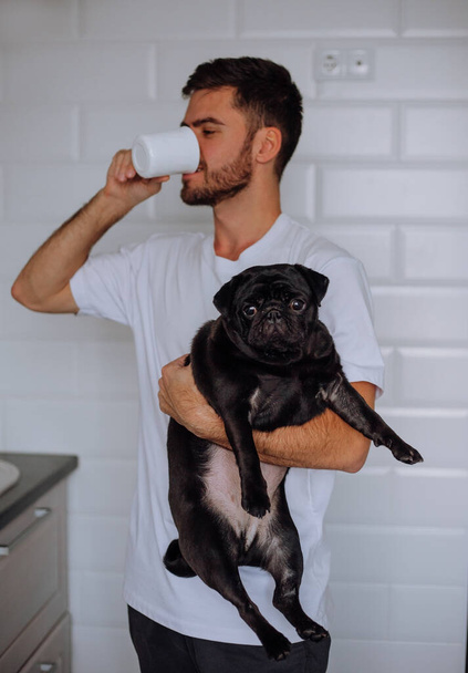 Un uomo tiene in braccio un cane carlino e beve caffè - Foto, immagini