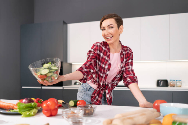 Happy holding bawl of salad young housewife cut tomato, cucumber, pepper for a family dinner or girls night standing in the kitchen. Healthy food living. Healthy lifestyle - Foto, Imagem