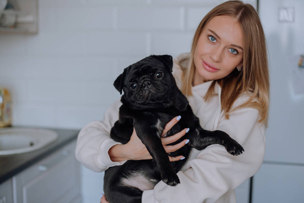 Girl holds a black pug dog in her arms at home - 写真・画像