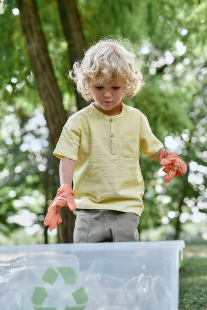 Lindo niño caucásico con guantes de goma recogiendo residuos de plástico en el bosque o parque, botellas de plástico en el reciclaje - Foto, Imagen