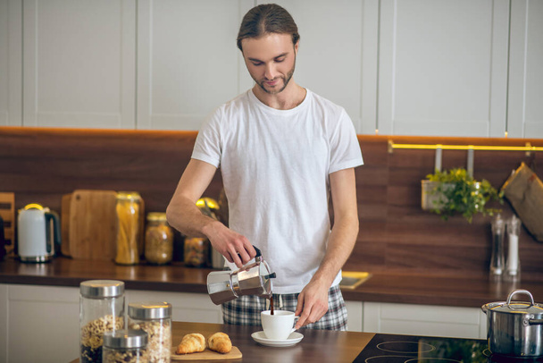 Mladý muž v homewear nalévání kávy do šálku - Fotografie, Obrázek