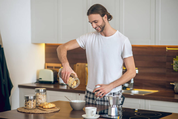 Young man in homewear pouring cereal to the bowl - Φωτογραφία, εικόνα