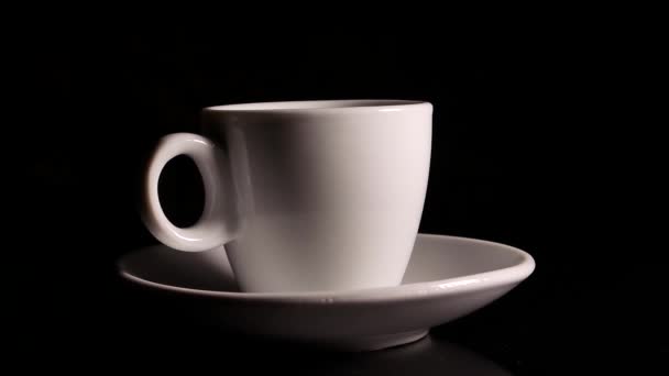 セラミックコーヒーカップは黒い背景で回転します。カップとソーサー。セラミック食器。コーヒーハウス。カフェだ。台所用品だ。熱い飲み物だ。黒の背景。円の中の回転。ビデオ. - 映像、動画
