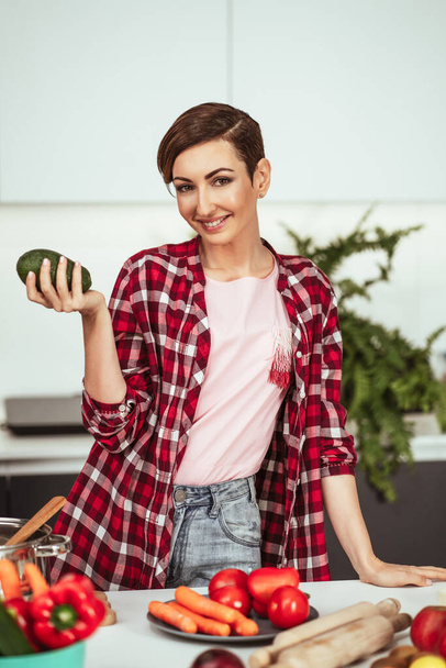 Fresh avocado in the hand of a pretty housewife with a short hairstyle prepares food in the kitchen. Healthy food at home. Healthy food leaving - vegan concept - Photo, image