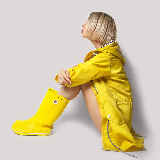 Young woman in slicker and rubber boots in colors Ultimate Gray and Illuminating - Foto, afbeelding