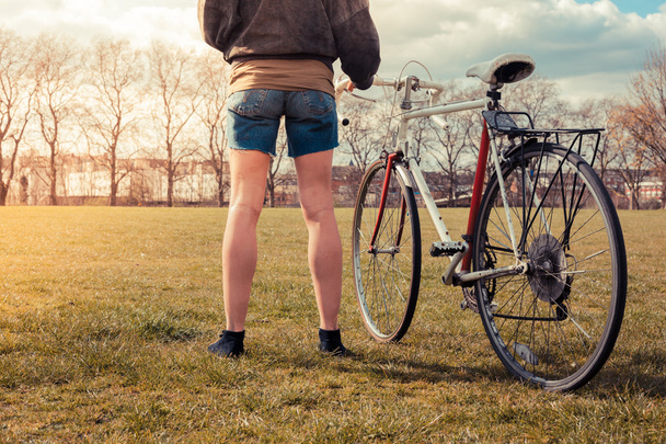 Jovem mulher de pé no parque com bicicleta
 - Foto, Imagem
