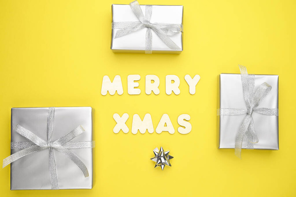 Gift box, gray decorations on yellow background and the words Merry xmas made of wooden letters. - Foto, Bild