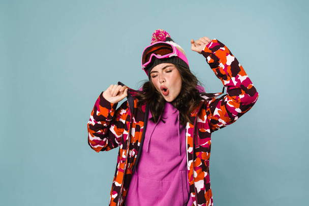 Excited young woman wearing snowboard jacket celebrating isolated over blue background - 写真・画像