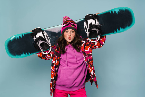 Happy sportswoman posing with snowboard isolated over blue wall - Photo, image