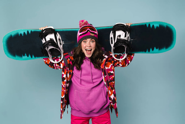 Boldog sportasszony pózol snowboard elszigetelt a kék fal - Fotó, kép