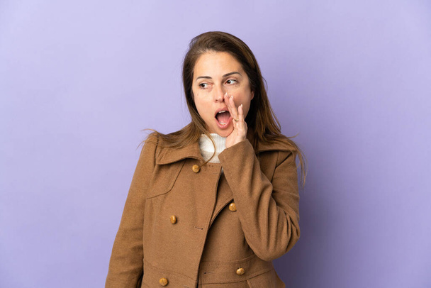 Middle age Brazilian woman isolated on purple background whispering something with surprise gesture while looking to the side - 写真・画像