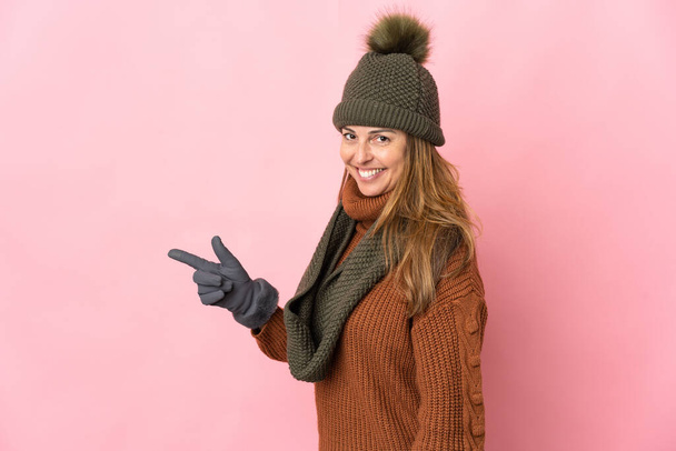 中年女性とともに冬の帽子隔離されたピンクの背景指差し指に側 - 写真・画像