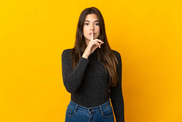 Teenager Brazilian girl isolated on yellow background showing a sign of silence gesture putting finger in mouth - Valokuva, kuva