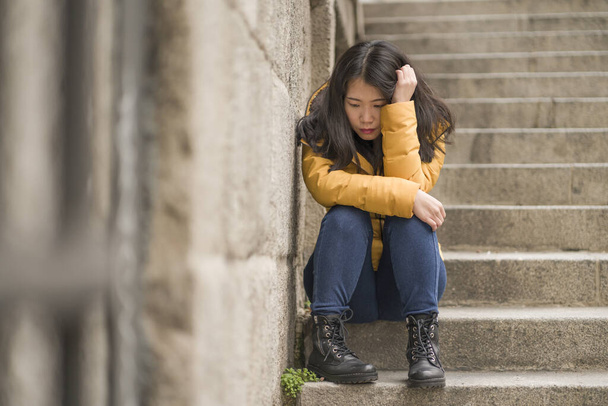 drámai életmód portré fiatal vonzó szomorú és depressziós koreai nő téli kabát ül a szabadban az utcasarkon lépcső szenved depresszió probléma érzés tehetetlen - Fotó, kép