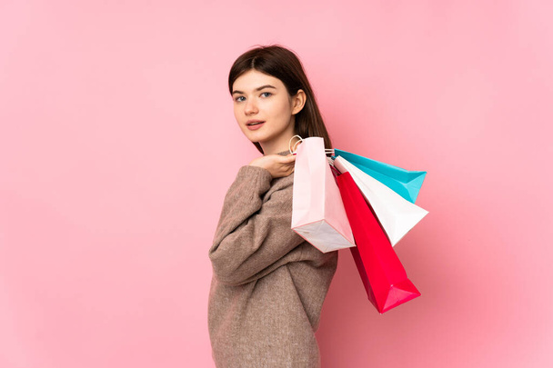 Young Ukrainian teenager girl over isolated pink background holding shopping bags and smiling - Fotó, kép